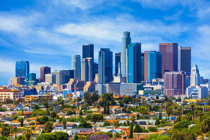 A bright view of Los Angeles skyline, featuring tall skyscrapers and vibrant residential buildings under a clear blue sky.