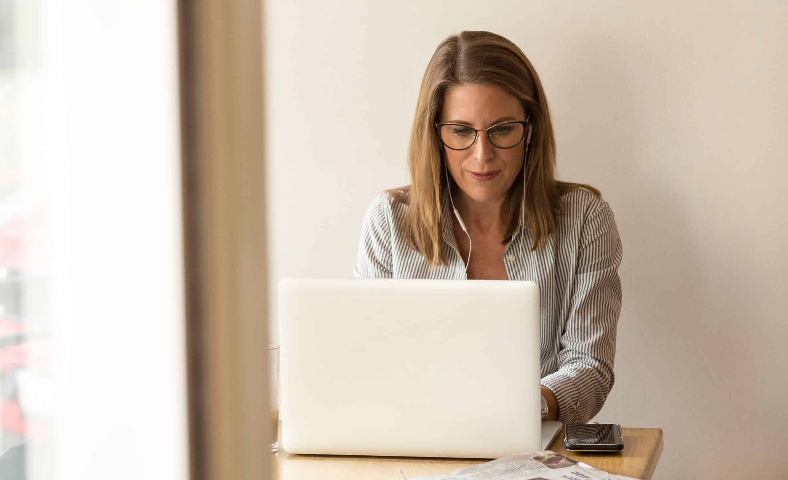 Woman in a striped shirt working on a laptop at a wooden desk.