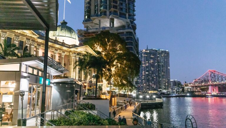 Twilight cityscape with illuminated buildings and a bridge over a river.