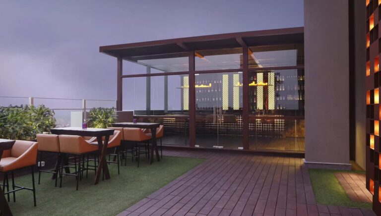 Rooftop patio with modern furniture, evening sky, and city lights in the background.