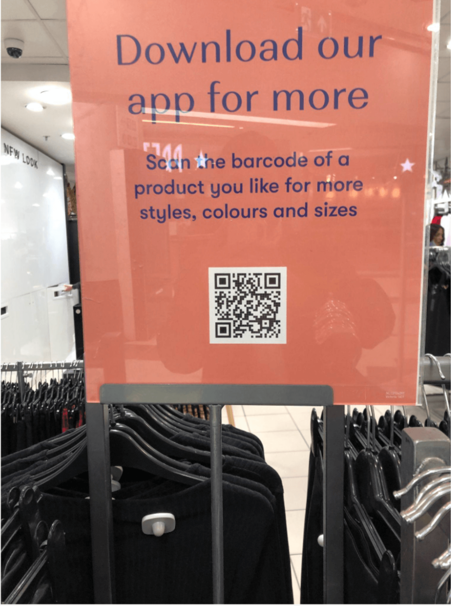 Picture of an in-store sign: "Download our app for more." The sign shows a scannable QR code to take shoppers to the app.