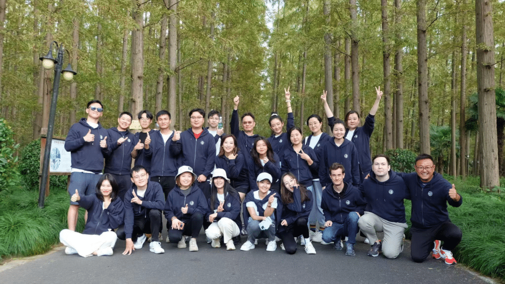 A group of Branch team members smile for a photo in a wooded area, all are wearing matching dark blue Branch sweatshirts and are facing the camera and smiling.