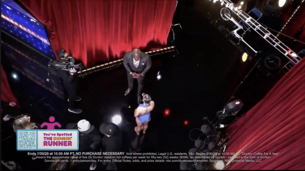 A behind-the-scenes shot of a television set featuring a host and a contestant preparing for a segment, with red curtains in view.