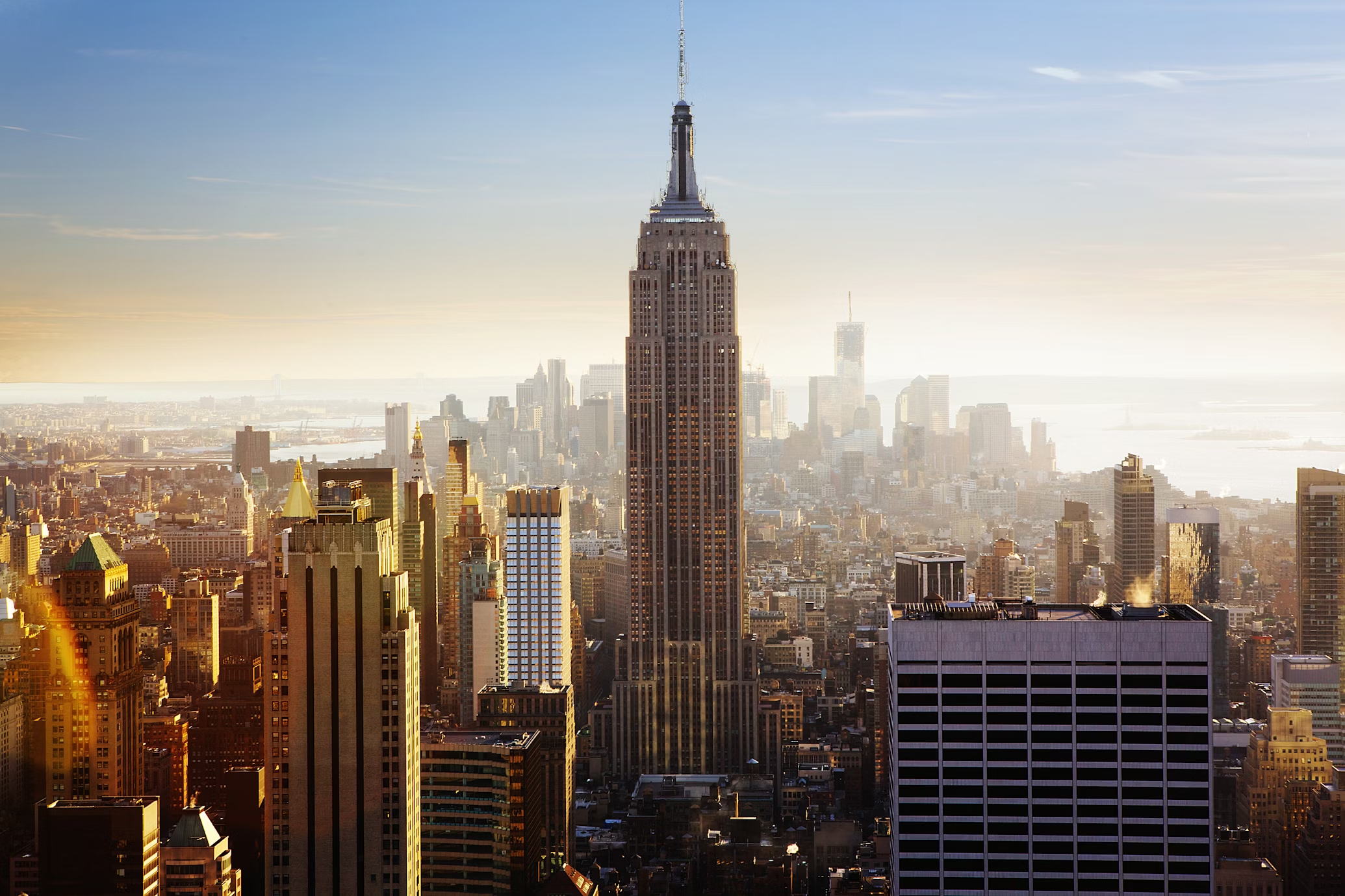 The iconic Empire State Building stands tall amid the New York City skyline bathed in golden sunset light.