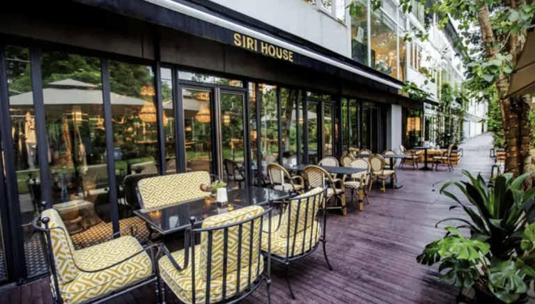Outdoor seating of SIRI HOUSE with patterned chairs on a wooden deck, surrounded by greenery.