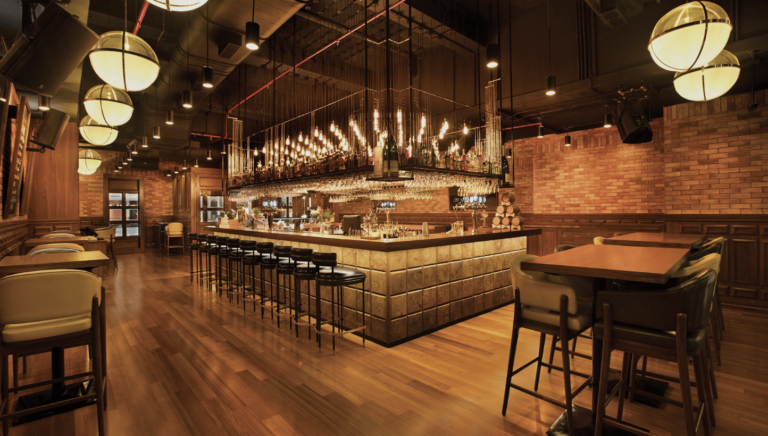 Dimly lit bar with stools and hanging globe lights, brick walls and a wooden floor.