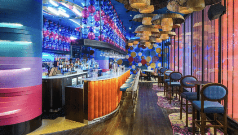 Vibrant bar interior with blue lighting, colorful hanging orbs, and a curved orange bar counter.